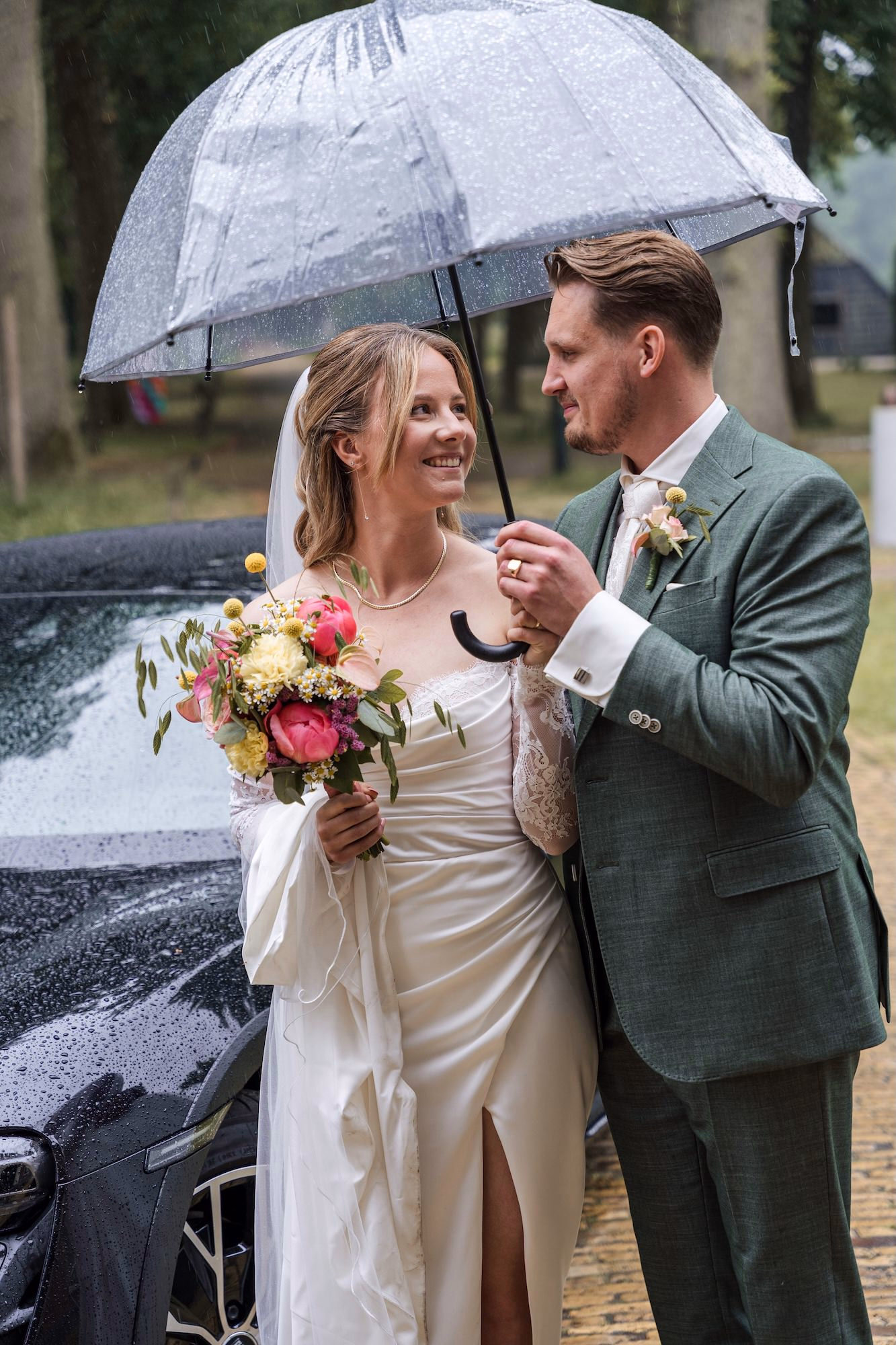 Trouwfotografie Zuid-Holland - Bruidspaar poserend voor de auto in de regen